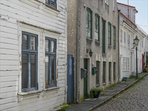 Historic white houses with red roofs along a narrow cobblestone street in daylight, white wooden