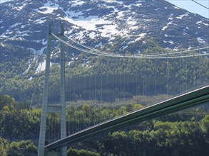 Bridge against a backdrop of snow-capped mountains and green forests under a clear blue sky, bridge
