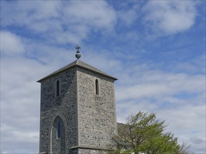 Stone church tower surrounded by a tree and a partly cloudy sky, old stone church and many