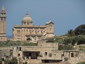 Neo-Romanesque basilica with visible ruins and surrounding vegetation under a blue sky, isolated