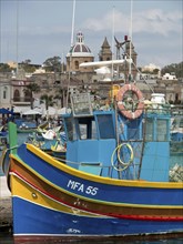 A colourful fishing boat in the harbour in front of a coastal town with a church in the background