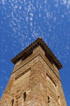 Bottom view of a large brick tower with a cloudy blue sky in the background