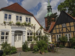 A white house with a red tiled roof next to a traditional half-timbered house under a blue sky with