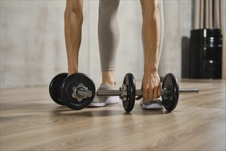 Closeup view of muscular female arms lifting dumbbells from the floor