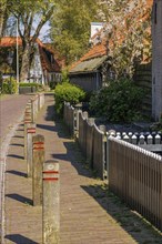 Quiet footpath along a wooden fence, lined with brick houses and trees in a village, historic