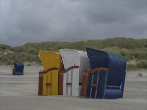 Colourful beach chairs standing one behind the other on a sandy beach under a cloudy sky, colourful