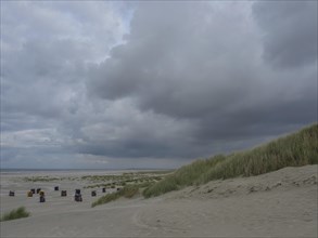 A cloudy beach with dunes and scattered beach chairs, a calm and cloudy atmosphere, colourful beach