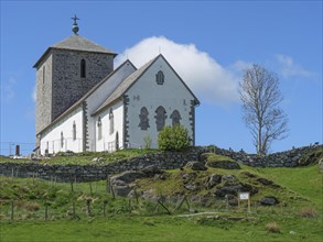White church with stone tower on a rocky hill under blue sky with clouds, old stone church and many