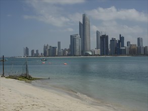 A beach with a view of a modern city with skyscrapers by the sea under a cloudy sky, impressive