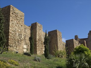 Medieval fortress with high stone walls and cypresses on a green area under a blue sky, stone walls