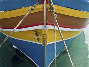 Colourful bow of a boat moored with ropes, on calm water in the harbour, many colourful fishing