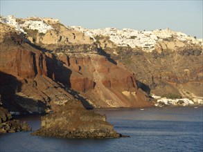 The steep coastal cliffs of Santorini in warm golden light, lined with white houses and rocky