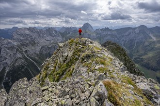 Mountaineer in front of a mountain landscape with rocky peaks, at the summit of the Raudenspitze or