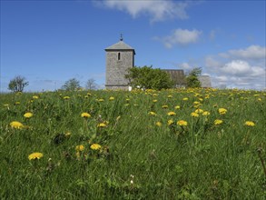 Stone church on a green meadow covered with dandelions under a blue sky with few clouds, Stone