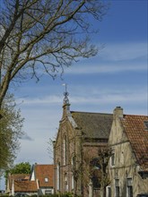 Church with weather vane and trees, house with red roof under blue sky, historic houses on a small