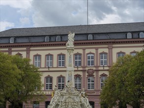 Baroque building with impressive statue in the foreground, surrounded by trees, under a slightly