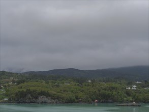 Landscape with remarkable green hills, houses and cloudy sky over calm water, greenish shimmering