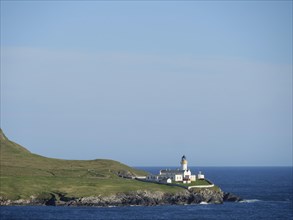 Lighthouse on the coast, surrounded by wide grassy areas and blue sea under a clear sky, white
