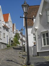 White wooden houses along a cobblestone street, streetlamp under a blue sky, historic architecture