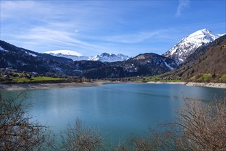 Lake Lungern surrounded by snow-capped mountains and green hills under a blue sky, Lungern,