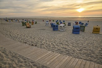 A quiet beach at sunset with colourful beach chairs, a wooden walkway and soft sand, lots of