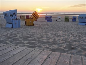 Various beach chairs on a sandy beach during sunset, sea in the background and a wooden walkway in