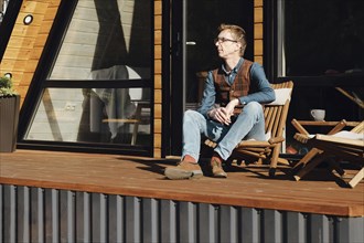 Middle-aged man enjoys warm autumn morning sitting on terrace of summer house