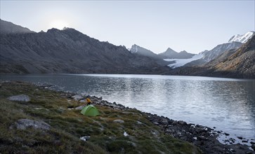 Mountain landscape with glacier tongue at Ala Kul mountain lake, green tent camping in the