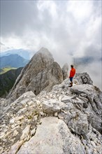 Mountaineer on a rocky narrow summit ridge, cloudy mountain peak, summit of the Great Kinigat,