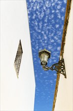 View of a streetlight between two streets with white walls and blue sky with clouds in the