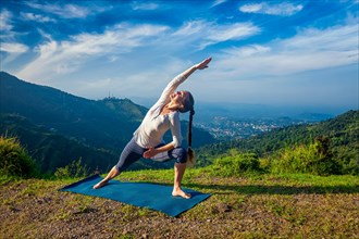 Woman practices yoga asana Utthita Parsvakonasana, extended side angle pose outdoors in mountains
