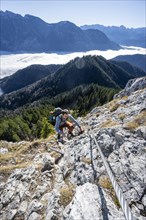 Hiker on via ferrata to Ettaler Manndl, view over mountain landscape and sea of clouds, high fog in
