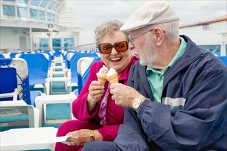 Happy senior adult couple enjoying ice cream on the deck of a luxury passenger cruise ship