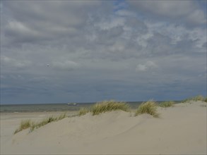 Sand dunes with a view of the sea and cloudy sky in the background, dune with dune grass and a boat