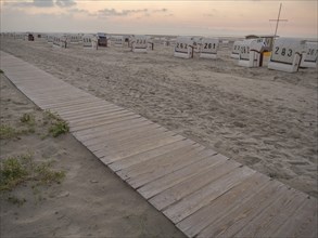 Wooden path to the beach with empty beach chairs and quiet atmosphere at dusk, setting sun on a