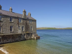 Old stone building near a sandy beach with clear blue water and blue sky in the background, old