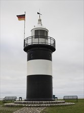 Black and white lighthouse, called 'Kleiner Preusse', at the sea, with German flag, flag waving in