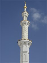 Tall white minaret with golden decorations and clear architectural design under blue sky, beautiful