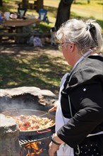 Woman cook seen in profile preparing a typical Spanish paella on the fire in the field