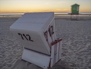 A single white beach chair on the beach at sunset, in the background a green beach hut, sunset on a