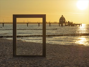 A picture frame on the beach with a view of a pier and the sea at sunset, sunset on a beach with a