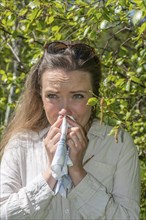 Young Caucasian woman, 35 years old, with allergy stands by flowering birch (Betula) in Ystad,