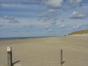 Wide, quiet sandy beach with posts in the foreground under a cloudy sky, clouds on the beach with