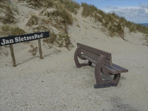A bench by the sand dunes, next to it a sign with the inscription 'Jan Sietsepad', on it a partly