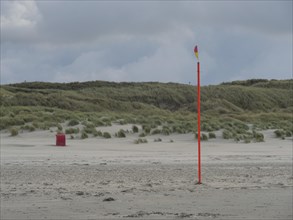 A lonely flagpole stands on a sandy beach in front of a hilly dune landscape, colourful beach