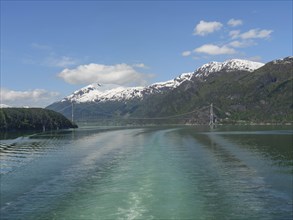 A bridge stretches across the water, surrounded by snow-capped mountains and clear sky, bridge in a