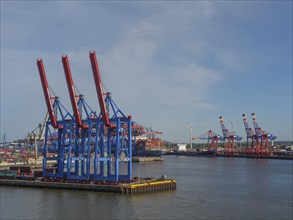 Container harbour with blue and red cranes, container ships and a cloudy sky, cranes and ships in a