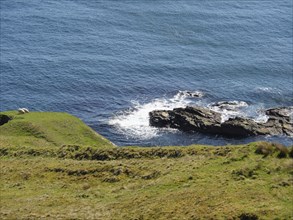 Hilly coastal landscape with grass and rocks sloping down to the blue sea, green meadows on a deep