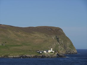 Lighthouse on the coast, surrounded by hills and blue sea under a clear sky, white lighthouse, on a