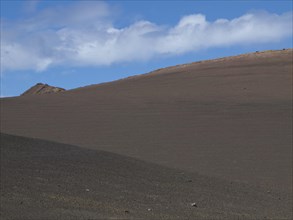 A sandy hill under a clear, slightly cloudy sky, barren landscape with roads, craters and small